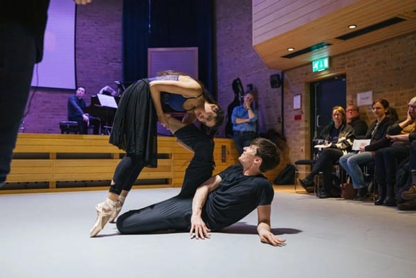 photo of two dancers on the JdP dancefloor during a past performance. Audience can be seen at the sides watching on, and musicians in the background on the stage