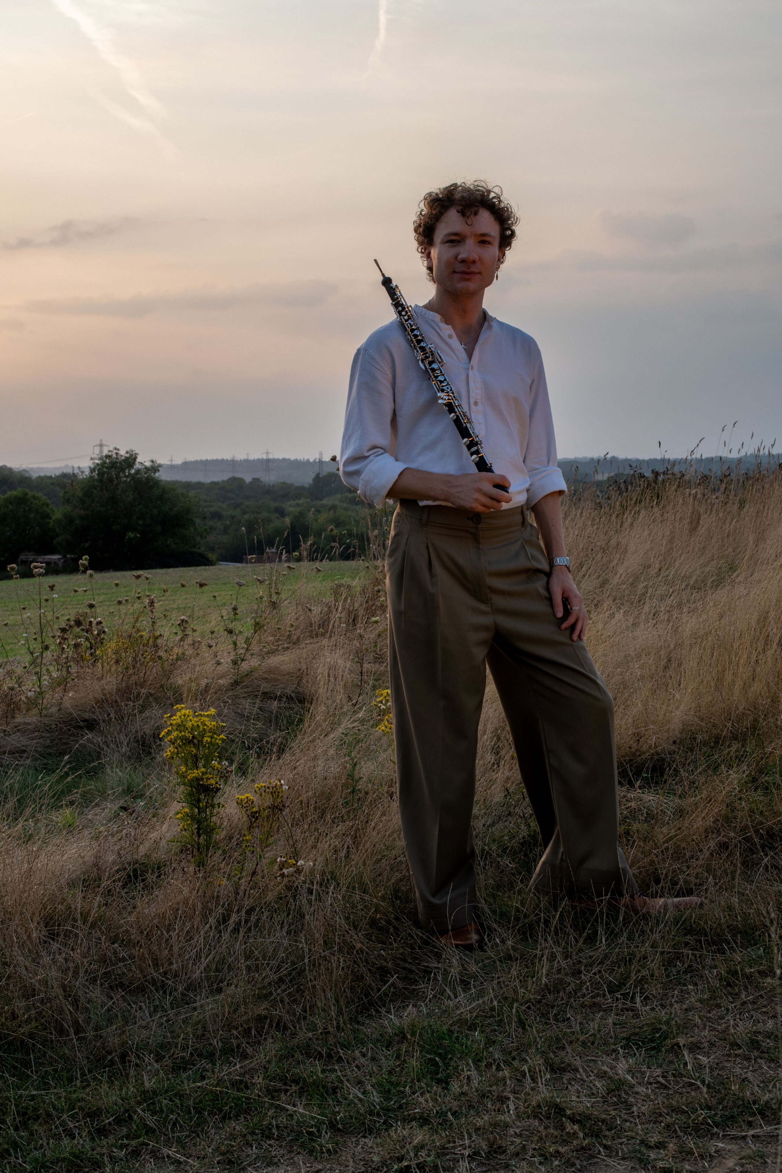 Ewan Millar, holding an oboe, standing in a field