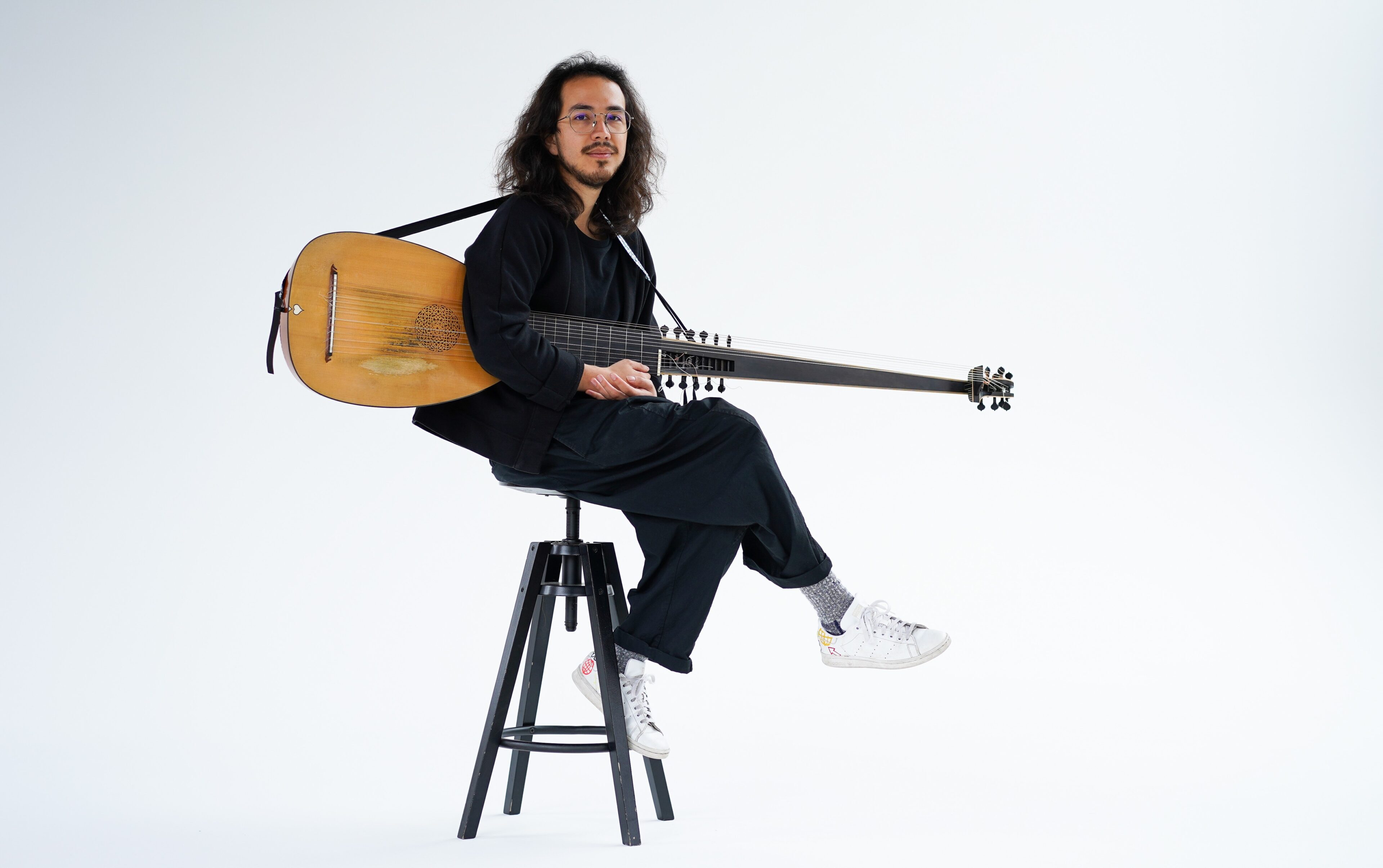 Sergio Bucheli sat on a stool holding a lute on a white background